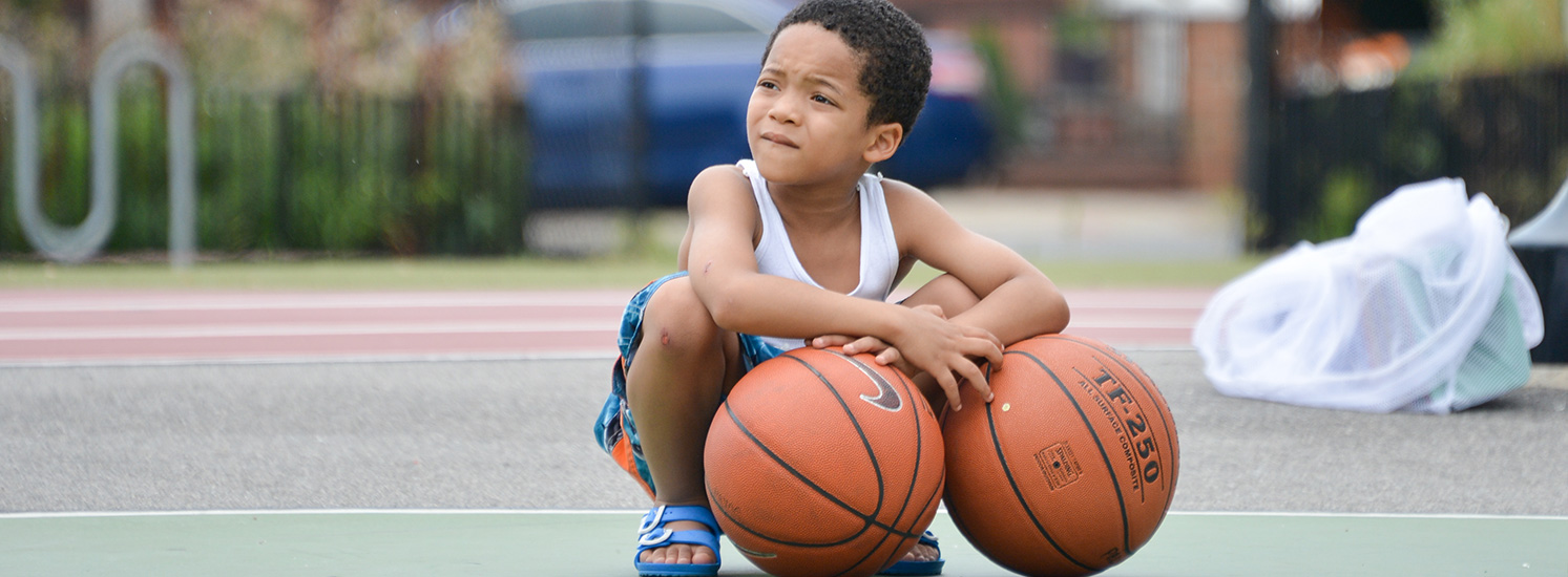 A young boy squats over a pair of basketballs on a court.