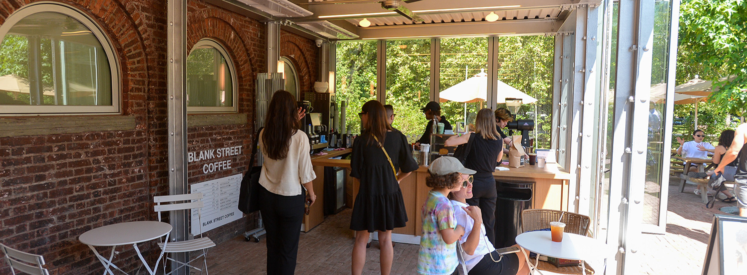 People gather in line to order from a coffee stand in a park.