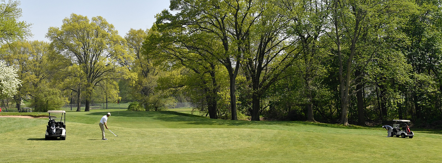 A golfer sets up for a shot next to their golf cart.