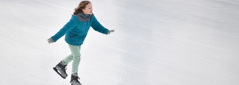 A young girl in skates smiling while on the ice.