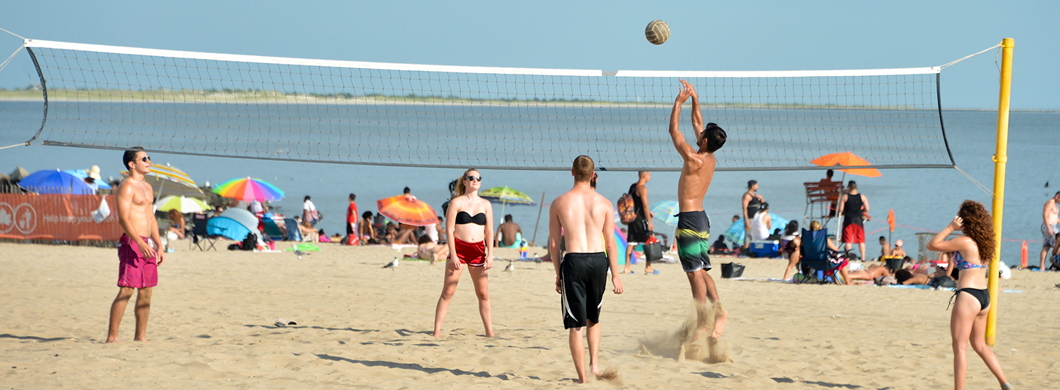 A group of mixed gender competitors enjoying a game of beach volleyball.