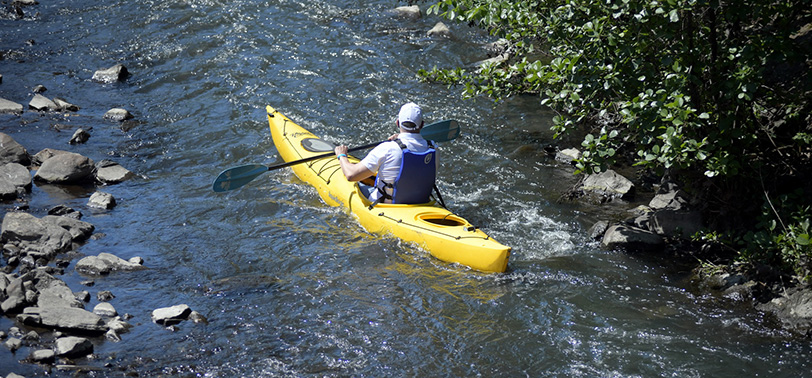 A paddler seated in a kayak navigating along a river.