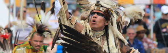 men dressed in traditional Native American wear participates in a dance in the park