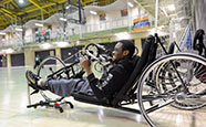 A patron at an adaptive hub uses and accessible cycling equipment to work out at the indoor gym