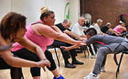 an instructor leads a class in a series of modified yoga moves performed while participants sit in chairs