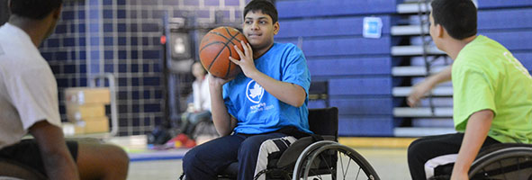 A kid holding a basketball looks to pass the ball to a teammate in a game of wheelchair basketball