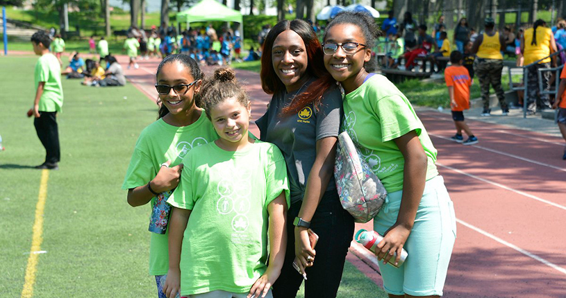 Campers pose for a photo with their camp counselor at an outdoor sports event in the park.