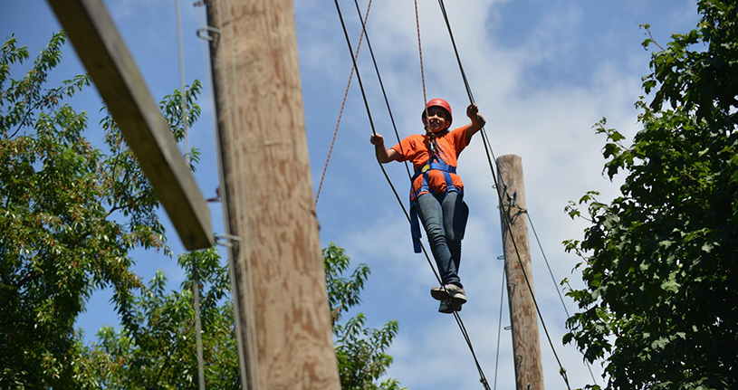 A camper tries out walking the elevated catwalk section of our ropes course at the Adventure Course in Alley Pond Park.