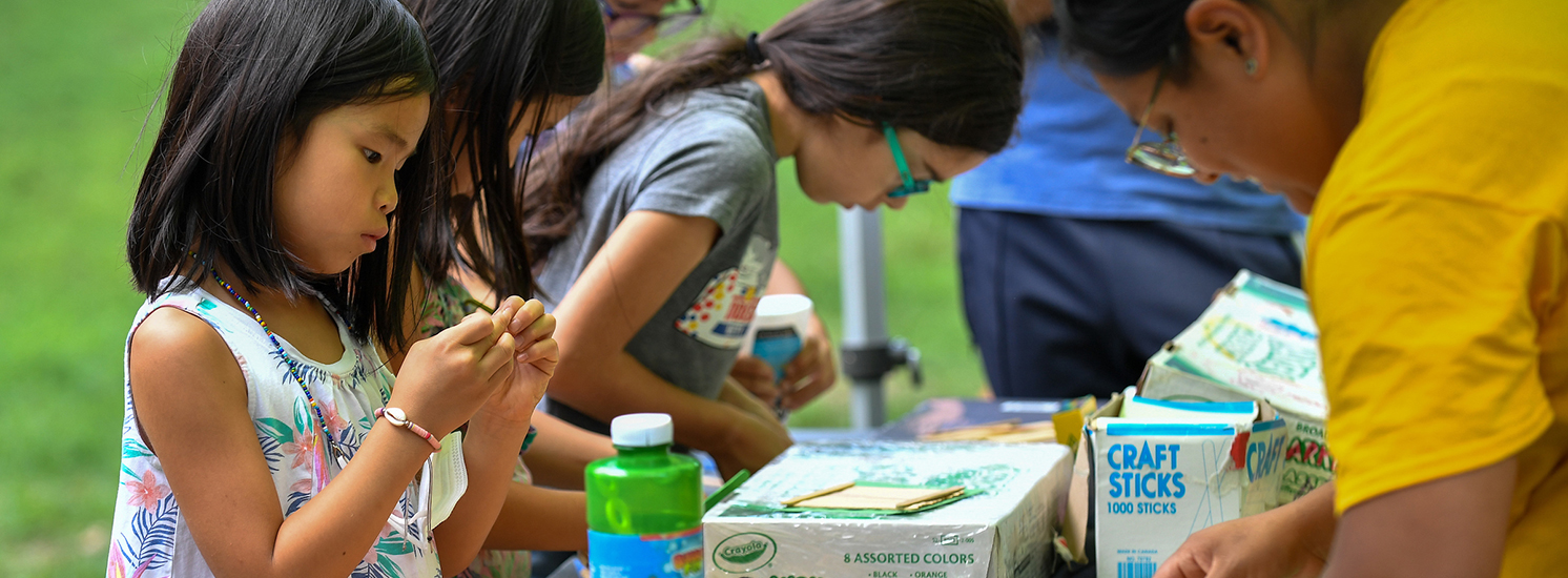 A determined young girl works on an arts & crafts project made of popsicle sticks.