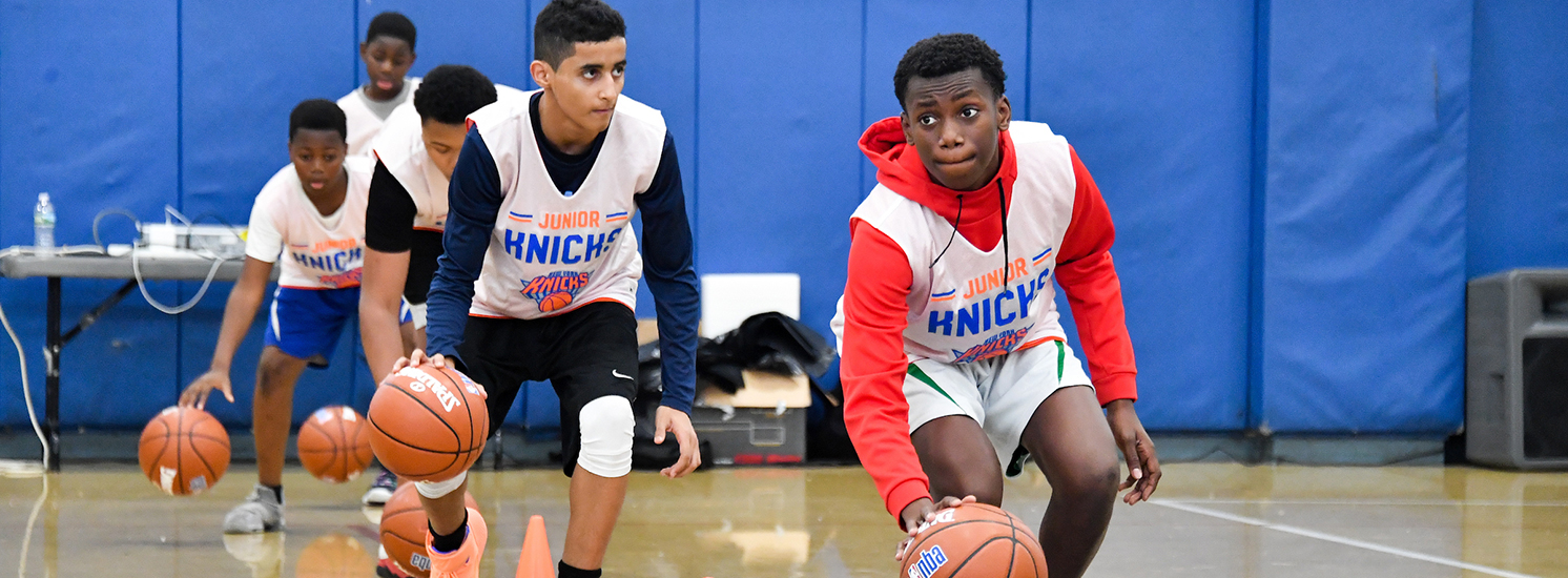 A line of teenage boys dribble basketballs around cones.