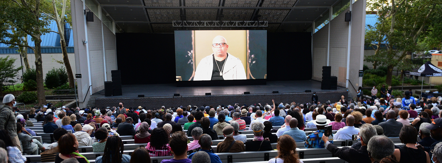 People sitting in an outdoor amphitheater, watching a movie together.