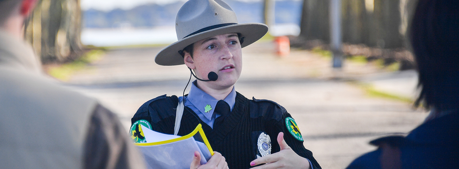 A ranger wearing a headset microphone appears to be explaining something to a crowd.