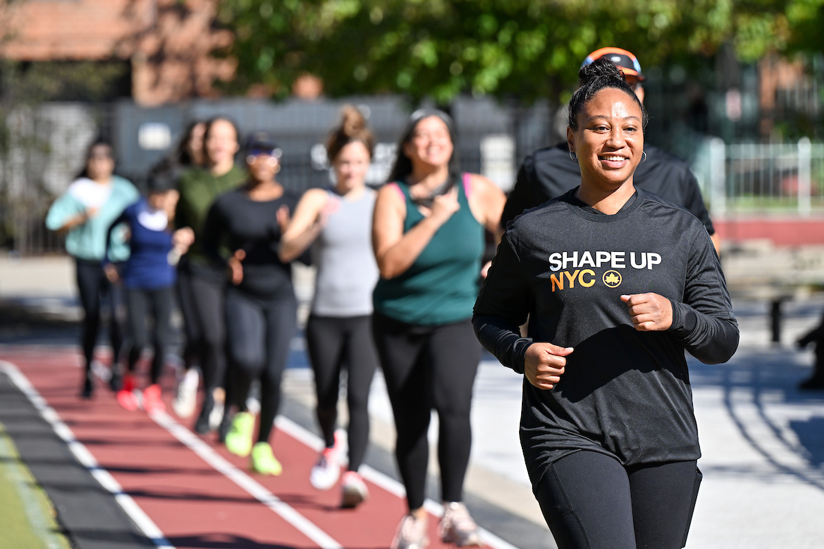 An instructor leads a group of people jogging on an outdoor runnings track.