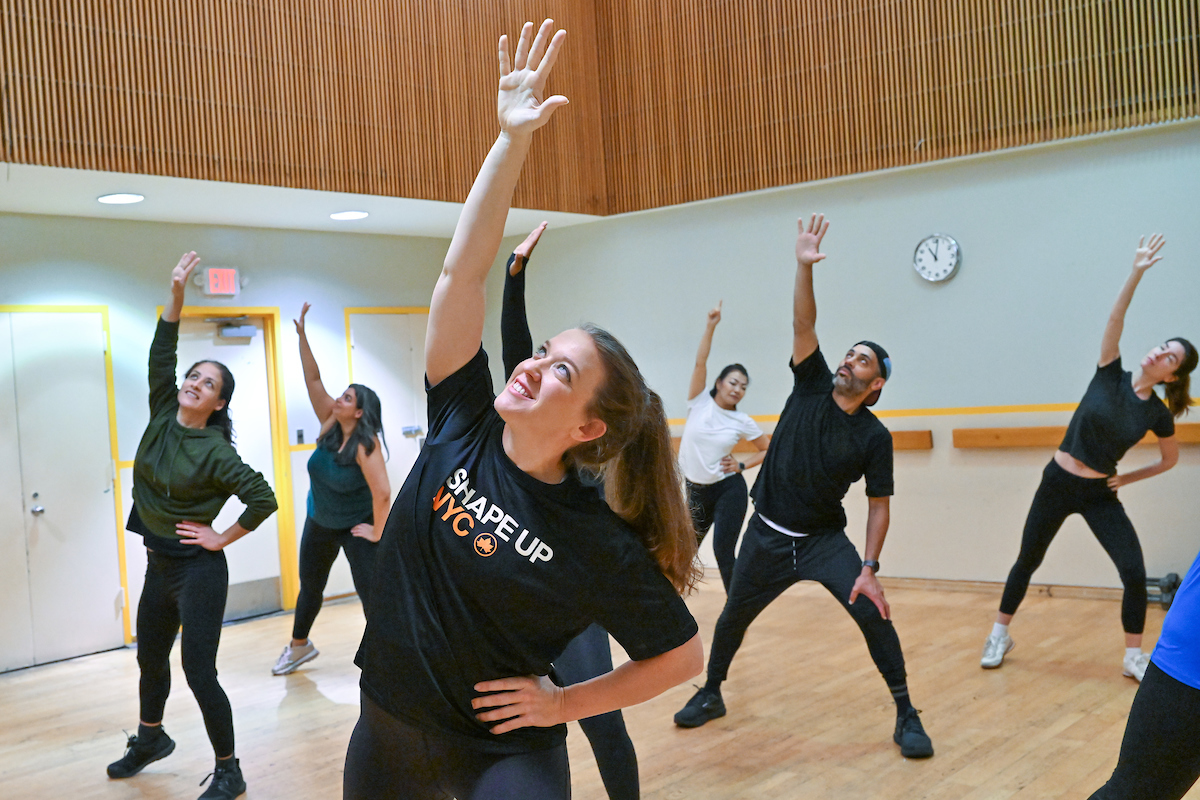 An instructor leads a group of people in an aerobics class with their hands raised.