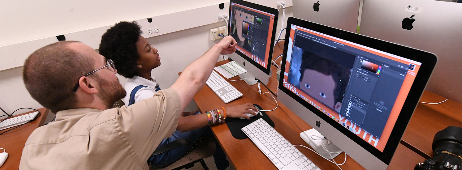 A student and teacher work on creating cartoon illustrations on computers.