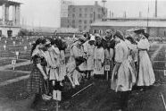 A class, mostly of girls, carefully observes its teacher during a lesson, circa 1905. 